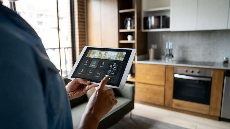 A man holding a tablet with a smart home control dashboard on its screen