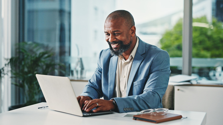 A person smiling as they work on a laptop