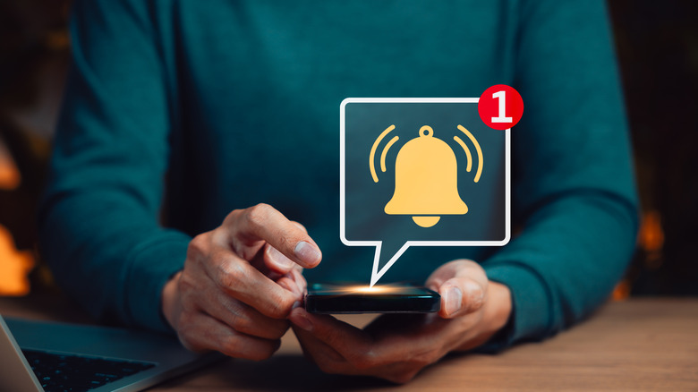 Close up of someone holding a smartphone with a bell icon floating above it with a 1 in the corner to represent a notification.
