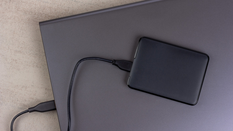 A closed laptop with a hard drive connected by a cable close-up on a gray background top view