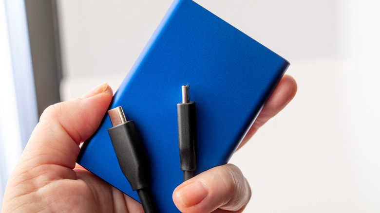 Hand holding slim blue power bank with cable. Lightweight external battery pack for mobile electronics.
