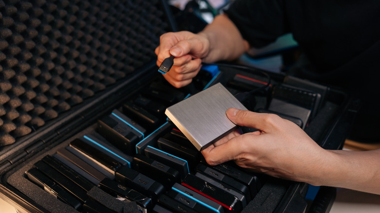 Person hands organizing external solid state drives and USB cable from protective storage case,