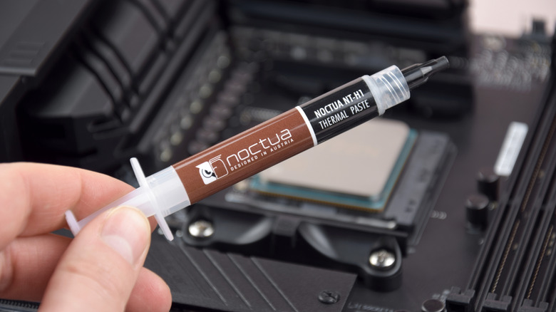 Syringe of Noctua thermal paste held above a CPU installed on a motherboard.