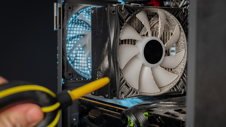 Person cleaning dust from a PC cooling fan with an air blower.