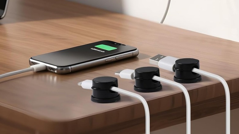 Three AGPTEK Magnetic Clip Cables are attached to the edge of a desk, each one holding a USB cable, a cellphone also sits atop of the desk
