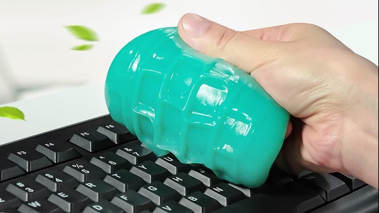 A hand using The TICARVE Dust Cleaning Gel to clean a black keyboard