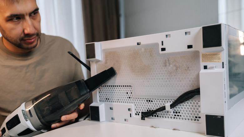 A man cleaning under a PC case with a vacuum cleaner.