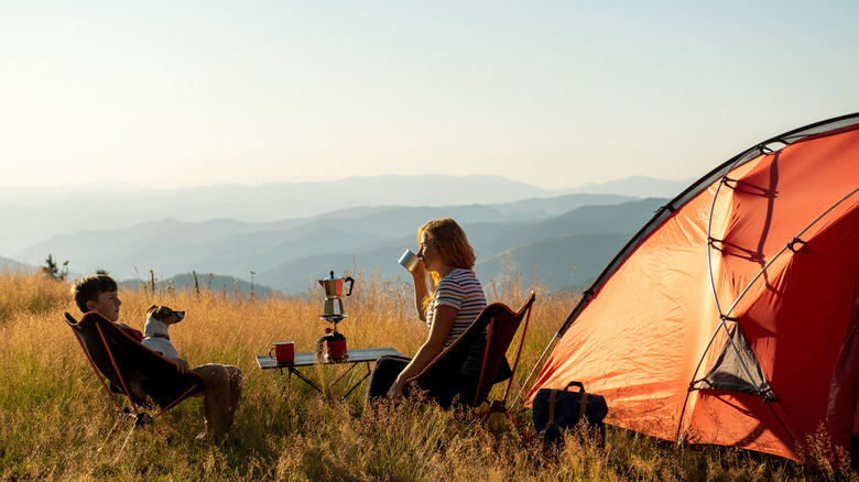 A couple resting in their mountain campground with a sunset in the background.