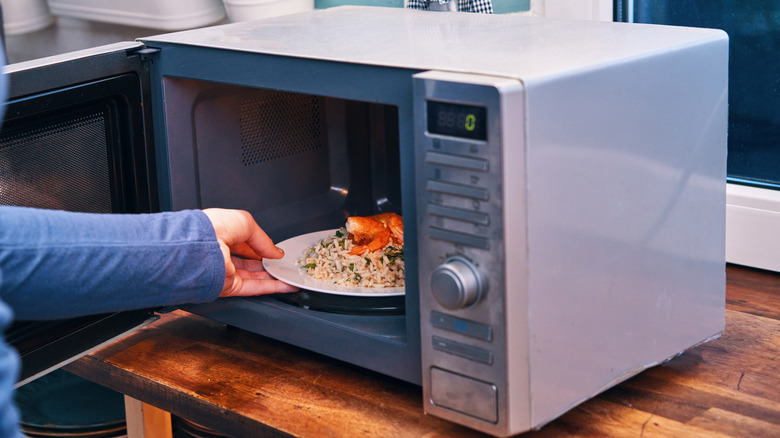 Person placing a plate of food inside a microwave.