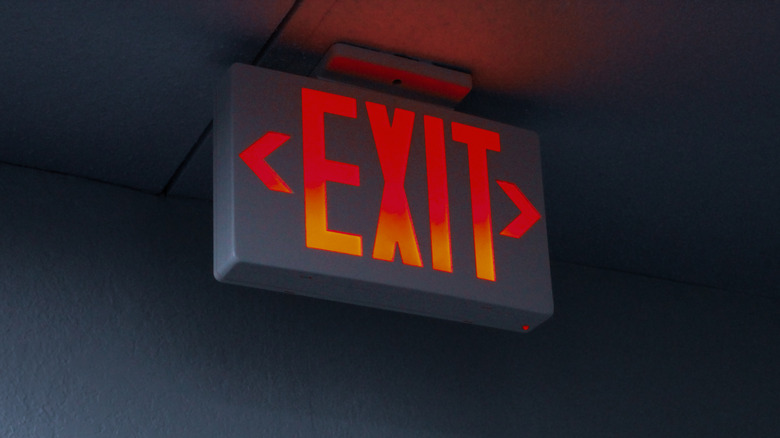 Red illuminated exit sign mounted near the ceiling in a dark room.