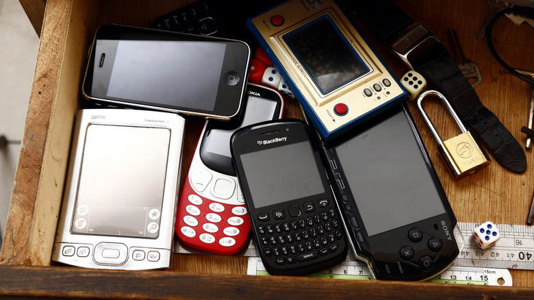 Vintage devices crammed in a drawer with a PDA phone visible.