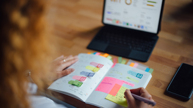 person working in a planner with a tablet open in background