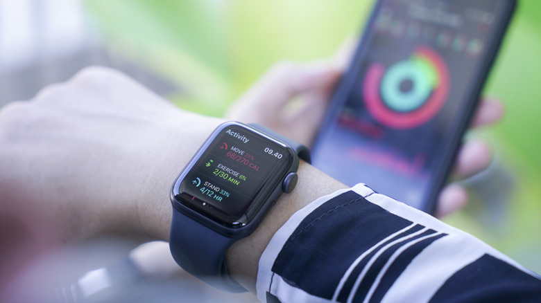 An Apple Watch on a wrist showing ring goals with a faded out iPhone in the background with the app.
