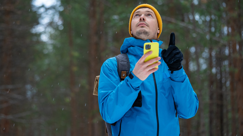 Hiker walking in the forest holding a yellow smartphone and looking up