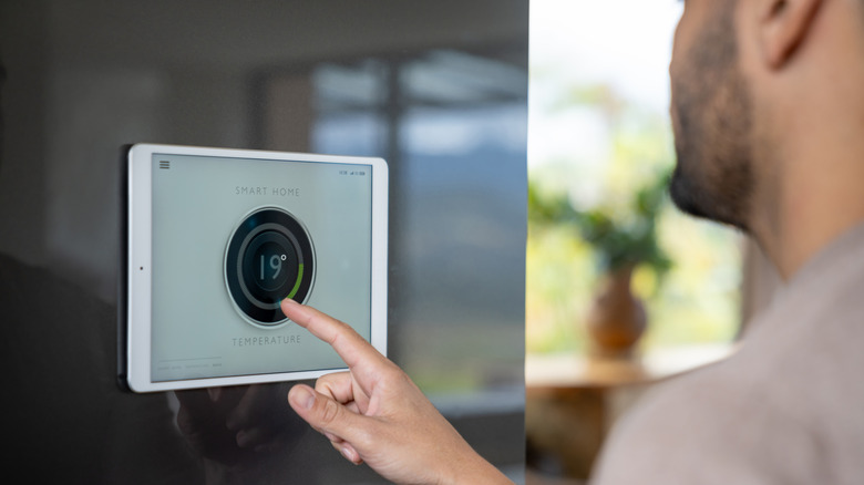 Person adjusting a smart home thermostat on a wall-mounted tablet.