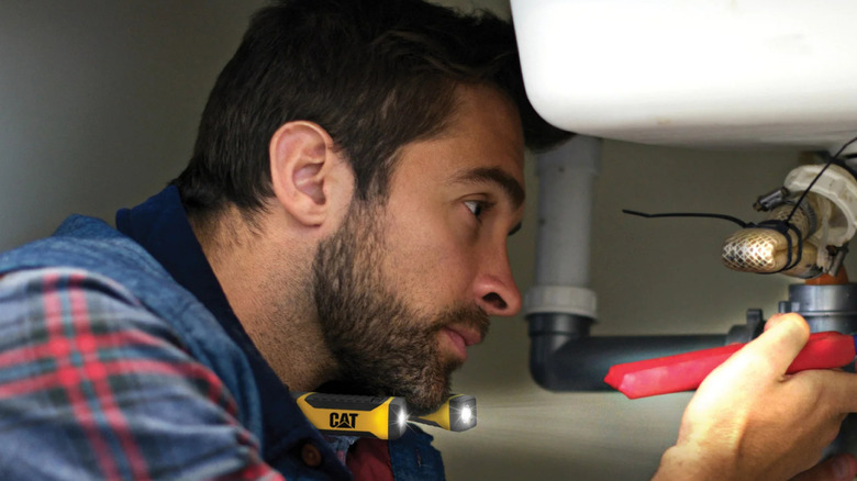 A man works on pipes with a CAT LED Neck Light.