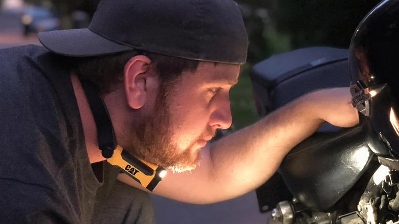 A man works on a car with a CAT LED neck light.