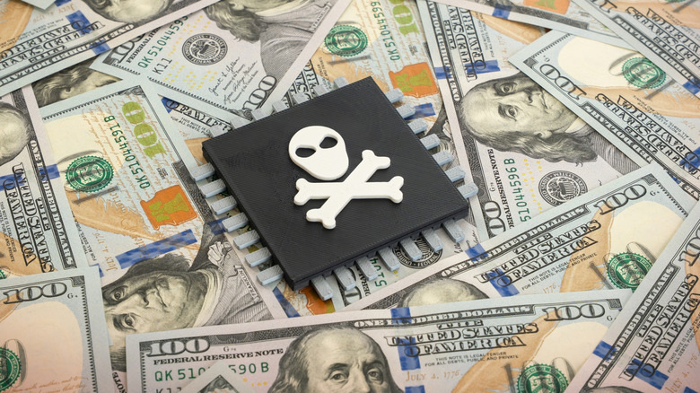 A seemingly 3D-rendered computer chip bearing a skull and crossbones sits on top $100 bills that have been meticulously laid out to cover the entire area of the photo