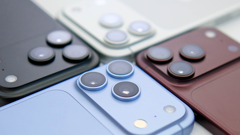 Four iPhone 18 models laying in a fashion that keeps all of their cameras centered in the image, the models are dark purple, blue, white, and black