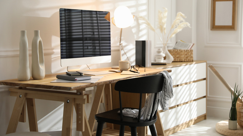 Bright home office desk with a desktop computer, lamp, chair, and decorative vases.