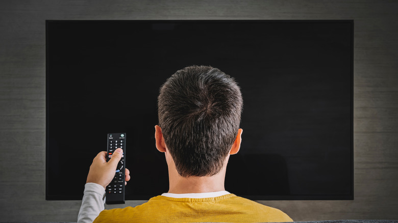 A man pointing a remote at a TV that's turned off.