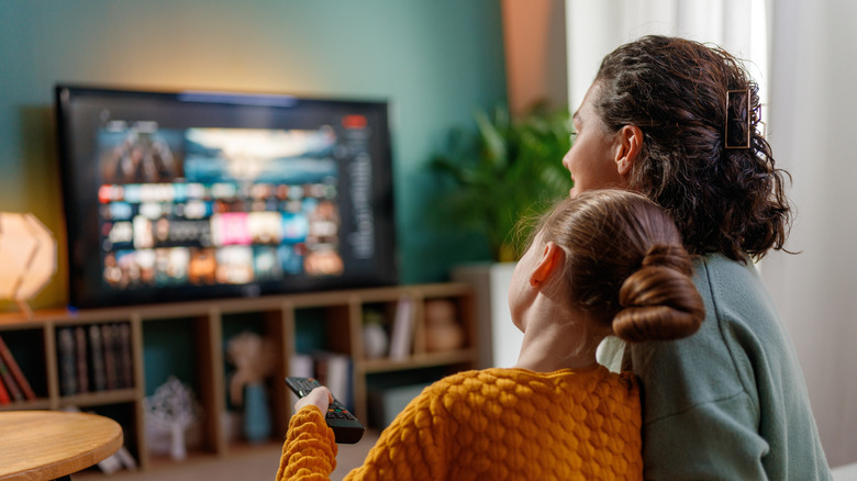 A mother and daughter watching TV together in a living room.