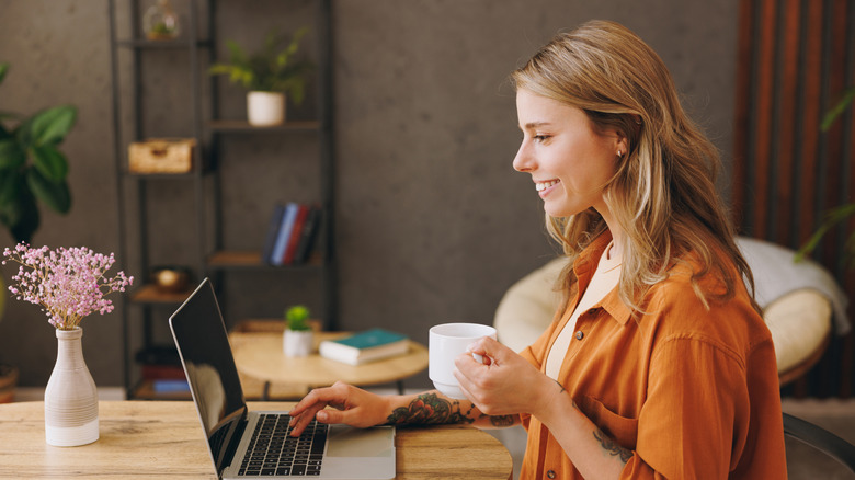 woman smiling at a laptop screen with a cup in hand