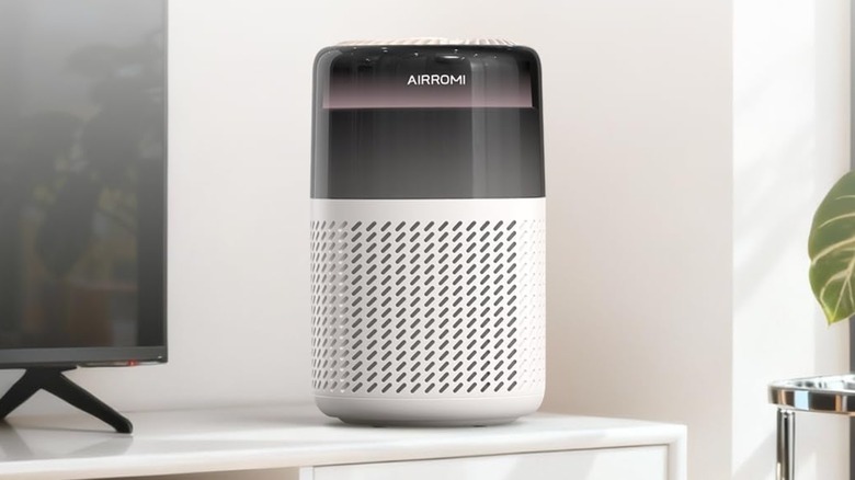 The Airromi HEPA Air Purifier for Bedroom sitting on a white TV stand between a television and a plant