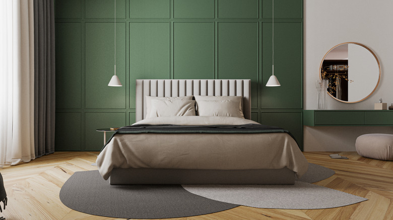 A clean, put together bedroom that has a green exterior along the back wall, with a bed in the center of the room that has light brown and dark blue bedding