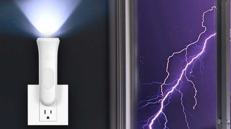 The Rossex 4-in-1 LED Emergency Light connected to an indoor power outlet, a nearby window shows there is lightning outside