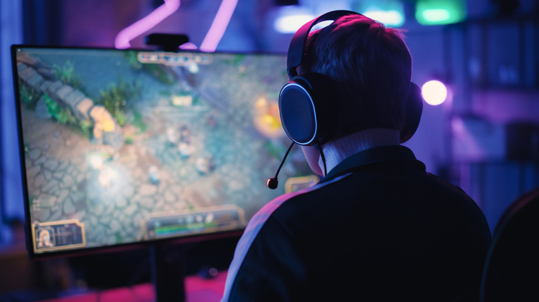 A user sits at a gaming monitor in a dark room, they're wearing a pair of black headphones with a microphone