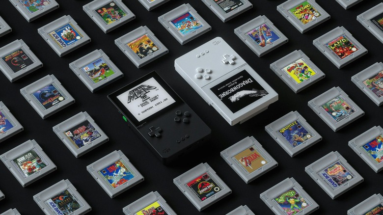Black and white Analogue Pocket handheld consoles surrounded by Game Boy cartridges