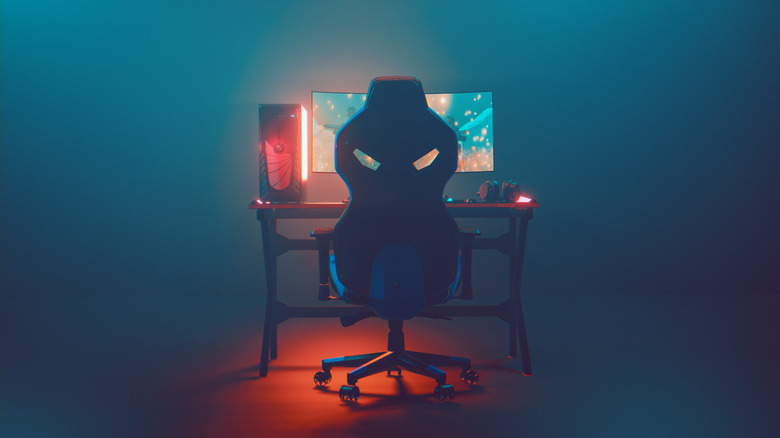 The neon glow of a gaming monitor fills a room with a desktop setup in view.