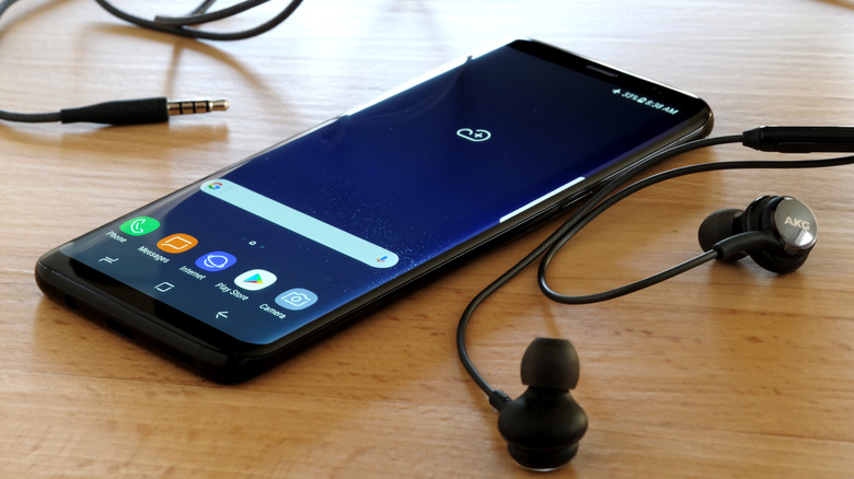 an old Samsung phone on a table next to a pair of ear buds