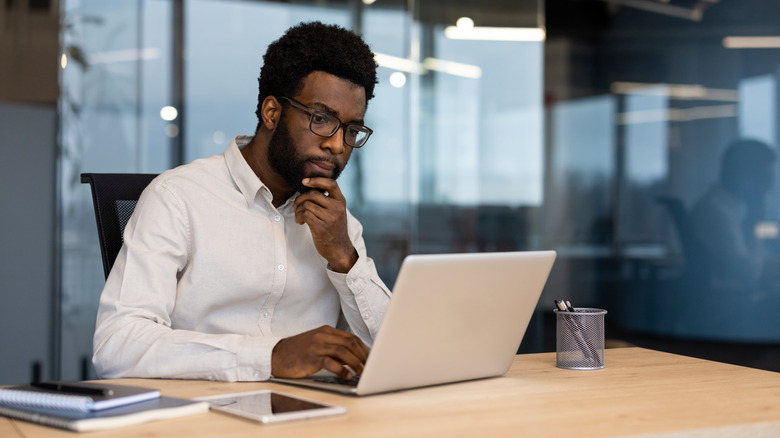 Serious-looking man with hand on chin staring down at laptop