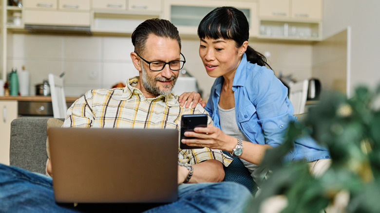 Couple using a laptop and a phone together while sitting on a couch