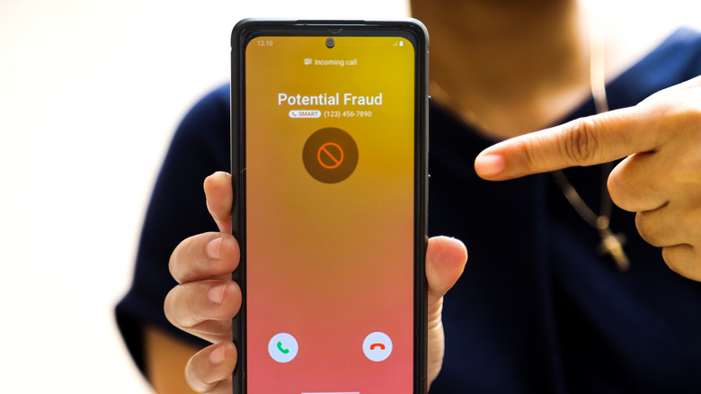 Woman holding phone showing fraud call on screen, while pointing at it