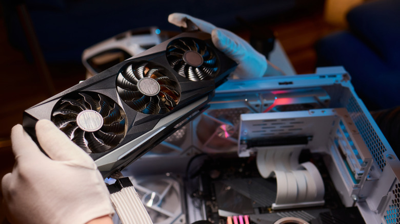 A gloved hand holding a graphics card while checking an open PC