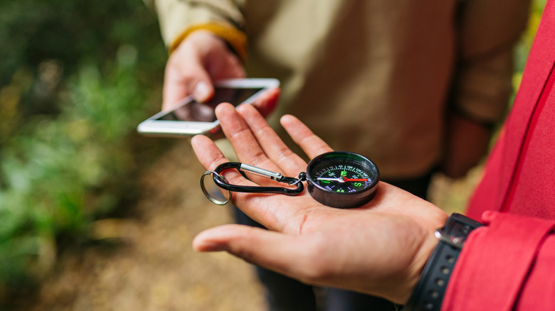 Compass and phone held in hands of hikers
