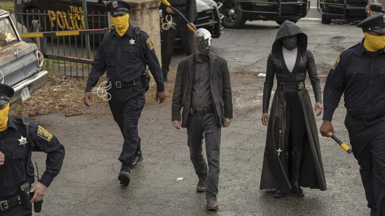 Sister Night (Regina King), Looking Glass (Tim Blake Nelson) and police walking in Watchmen
