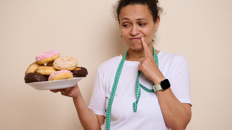 A woman wearing a smartwatch looking at a plate of donuts.