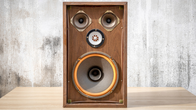 A vintage speaker sitting on a desk with a concrete wall behind it