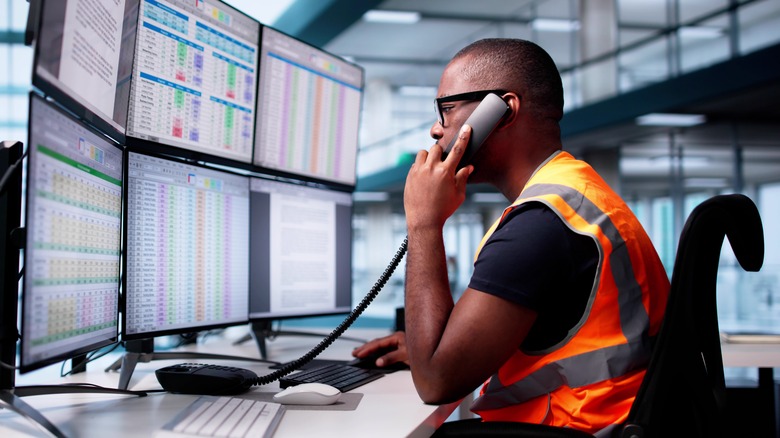 A man sitting in front of several PC monitors while taking a phone call.