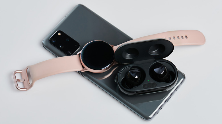 Smartwatch and earphones charging wirelessly on top of a smartphone