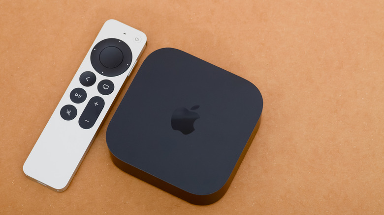 The Apple TV 4K placed next to its Siri remote on a wooden surface.