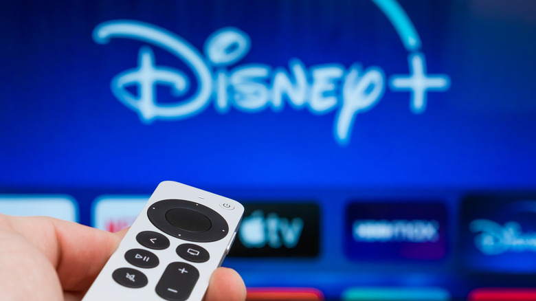 A person pointing a Siri remote toward a TV screen populated with apps.