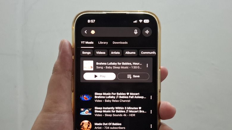 Hand holding phone showing baby emoji as search in YouTube Music