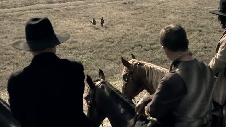 A group of men on horses look down at two men on horses in a field