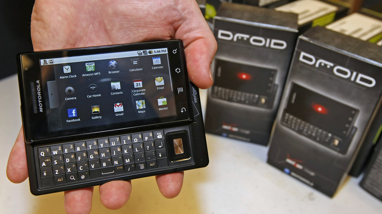 The Motorola Droid in a person's hand, with its product packaging boxes set behind.