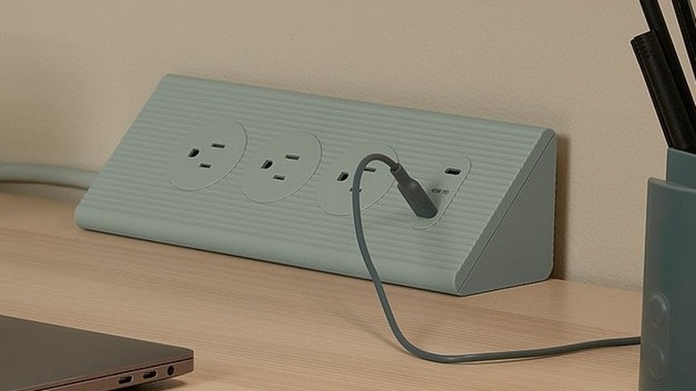 The Skotat Extension Cord placed in the corner of a desk with one USB cable plugged in